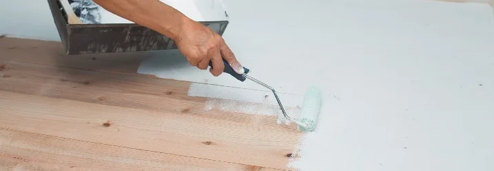 Person streicht Holzboden weiß